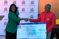Image of a woman shaking hands and handing over check to another woman.