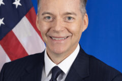 Image of a man, Ambassador Roger F. Nyhus, in front for an American Flag