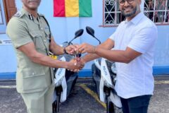 A man handing keys to a scooter to a Grenadian police officer