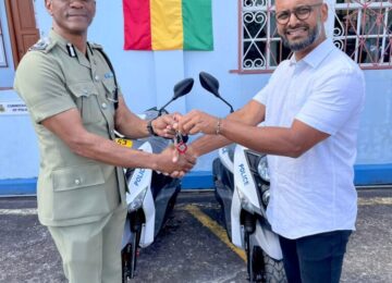 A man handing keys to a scooter to a Grenadian police officer