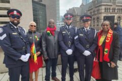 Image of a group of people standing at a flag raising ceremony at the Toronto City Hall with a Grenada flag