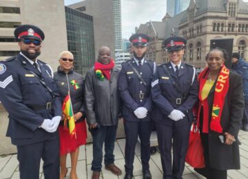 Image of a group of people standing at a flag raising ceremony at the Toronto City Hall with a Grenada flag