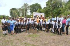 Officials and students pose beneath the signage for construction of the new Grenada Christian Academy School in Pearls, St. Andrew