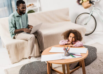 Image of Father working from home while looking after daughter.